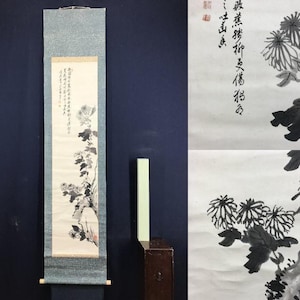 May include: An Asian scroll painting with a floral design in black and white ink. The artwork shows chrysanthemums with detailed leaves and stems. The scroll is mounted on a light blue fabric with wooden dowels.