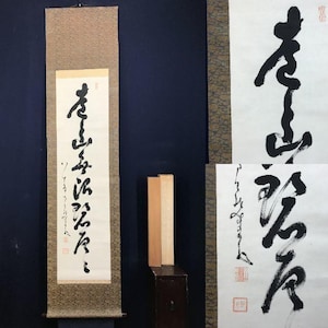 以下が含まれることがあります： クリーム色の紙に黒い書道が施された伝統的な日本の巻物。巻物は模様のある茶色の布に取り付けられています。さらに2つの書道作品と小さな木箱も表示されています。