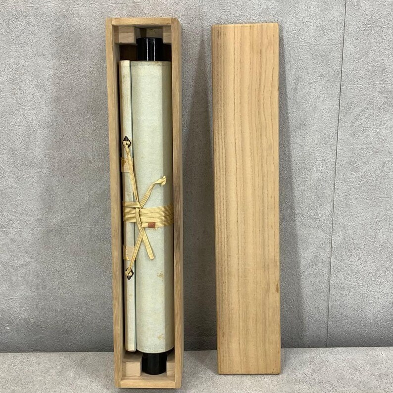 Puede incluir: Un rollo enrollado en una caja de madera. El rollo est&aacute; atado con un cord&oacute;n beige. La caja es rectangular y de madera clara. El rollo es blanquecino con detalles en negro. La caja est&aacute; abierta, revelando el rollo y su contenido.