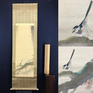 May include: An antique Japanese scroll painting featuring a bird perched on a branch with red leaves. The artwork is framed by a patterned border and has a wooden dowel at the bottom. The painting is displayed against a dark blue background.
