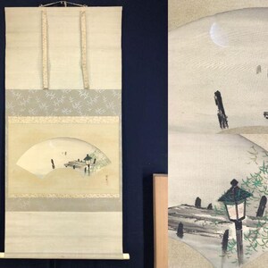 以下が含まれることがあります： 扇形の風景画が描かれた日本の掛け軸。 塔、三日月、人物が描かれています。 作品はベージュ、グレー、黒の落ち着いた色調で、装飾的な縁と吊り下げ用の紐が付いています。