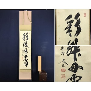 Pode incluir: Um pergaminho japonês vertical com caligrafia preta sobre um fundo creme, com a parte superior e inferior rosa. O pergaminho está pendurado em uma parede azul escura. Imagens adicionais em close-up mostram a caligrafia.
