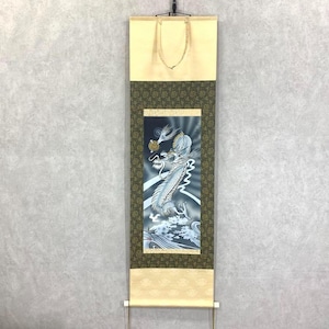 Könnte beinhalten: Japanische Rollbildmalerei mit einem weißen Drachen mit einer Goldmünze vor einem dunkelblauen und weißen Hintergrund. Die Schriftrolle hat eine cremefarbene Ober- und Unterseite mit einem dekorativen grünen Rand.