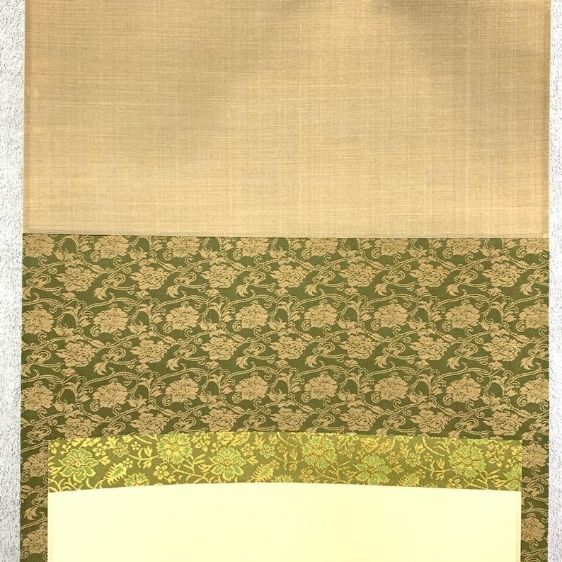 May include: A layered textile sample featuring a beige linen-like top section, followed by a section of olive green fabric with a floral pattern. Below is a strip of lighter green floral fabric, and a cream-colored bottom.