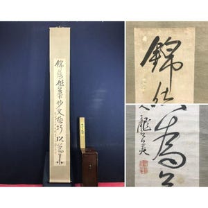 May include: A cream-coloured scroll featuring black calligraphy. The scroll is displayed vertically, with text running down its length. A small wooden box and a miniature wooden chair are next to the scroll. Close-up images of calligraphy are also included.
