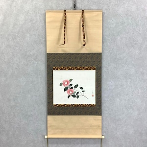 Op de afbeelding: Japans rolschilderij met een bloemmotief. Het kunstwerk toont roze cameliabloemen en groene bladeren op een witte achtergrond. De rol heeft een bruine rand en is omlijst door beige en bruin patroonweefsel.