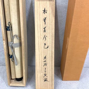 May include: A Japanese scroll painting in a wooden box. The scroll is tied with a patterned ribbon. The wooden box has Japanese characters written on it. An additional brown cardboard box is also present.