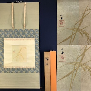 以下が含まれることがあります： 淡い緑色の背景、青い花の模様の縁取り、中央に麦の穂のデザインが施された正方形が特徴の日本の巻物絵画。巻物には下部に木のダボと吊り下げ用のリボンが付いています。
