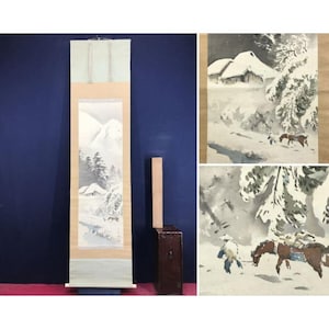 May include: A Japanese scroll painting showing a winter landscape with snow-covered mountains, trees, and a small house. The scroll is displayed vertically, with a light-coloured border and a blue background. Additional watercolour paintings of winter scenes are also shown.
