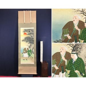 Op de afbeelding: Een antieke Japanse rolschildering met een landschap met figuren. Het kunstwerk toont een zonsondergang met een rode zon, bomen en figuren in traditionele kledij. De rol is omlijst in bruin textiel met crèmekleurige banden.