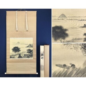 May include: A Japanese hanging scroll featuring a monochromatic ink wash landscape painting of a mountain, trees, and a person in a small boat. The scroll has a beige fabric border, two hanging ribbons, and a storage box with black ink calligraphy.