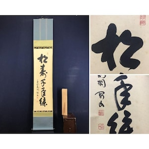 May include: A vertical scroll with calligraphy in black ink, featuring a light blue top and bottom section with a gold band. A wooden block rests on a small brown box. Two additional calligraphy pieces are also shown.