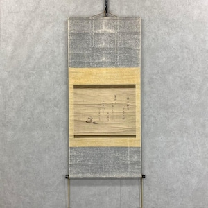Op de afbeelding: Een traditioneel Japans rolschilderij met een gedempt kleurenpalet. De rol bevat een centraal paneel met kalligrafie en een kleine illustratie van een vogel en rotsen. De boven- en ondersecties zijn lichtgrijs en de middelste sectie is lichtgeel.