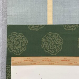May include: A section of a traditional Japanese scroll painting. The top portion features a light blue fabric, followed by a green fabric with a floral pattern. The bottom section has a landscape painting with a white background.