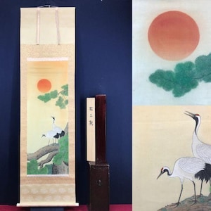 以下が含まれることがあります： 夕焼けを背景に、木の枝に止まっている2羽の鶴を描いた日本の巻物絵。黄色、緑、赤の色合いを使用。巻物は縦に表示されています。側面には日本語のテキストがあります。