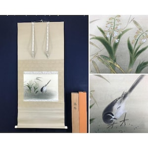 May include: A Japanese scroll painting depicting a bird amidst bamboo. The artwork is framed with a decorative border and has hanging cords. The scroll is presented with wooden storage boxes. The painting is in the traditional style.