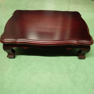 May include: A rectangular, dark cherry-stained wooden coffee table with a scalloped edge and four curved legs. The table has a glossy finish and sits on a green surface.