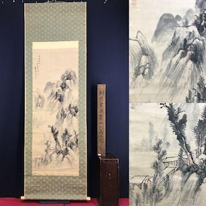 May include: An antique Asian scroll painting depicting a mountainous landscape in shades of gray and black. The scroll is framed with a green patterned border. A wooden, rectangular object with vertical text stands to the right.