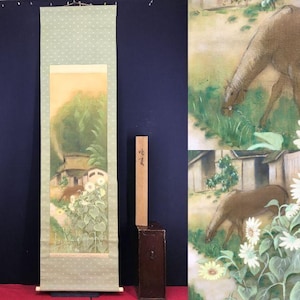 May include: A Japanese scroll painting showing a rural scene with a brown animal grazing near a house and sunflowers. The scroll has a light green top with white polka dots and a rectangular painting in the centre.
