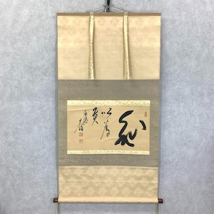 May include: An antique Japanese scroll painting featuring black calligraphy on a tan backdrop. The scroll has cream-coloured top and bottom sections with a floral pattern, and a tan middle section. It is suspended from a metal rod.