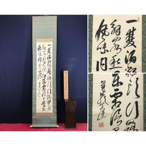 May include: An antique Japanese scroll with calligraphy in black ink on cream-colored paper. The scroll is displayed with a wooden box and a separate panel with additional calligraphy. The scroll has a blue and green patterned border.