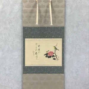 May include: Japanese scroll painting depicting a bird on a branch with a pink flower. The artwork includes Japanese calligraphy and is framed by patterned fabric in shades of grey and beige. The scroll is suspended by white ribbons.