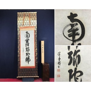 May include: A vertical hanging scroll featuring black ink calligraphy on a white paper background, framed by a dark blue and gold patterned fabric border. The scroll includes a wooden storage box with Japanese text and two red ink stamps.