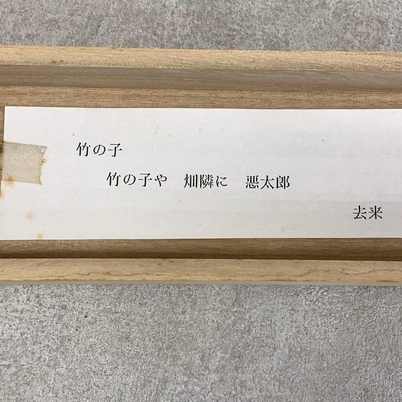 May include: A rectangular wooden frame with a white paper insert. The paper has Japanese text in black ink. The text includes the words "竹の子" and other Japanese characters. The paper is slightly yellowed with age.