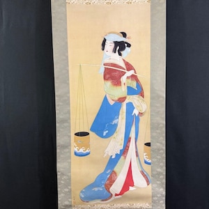May include: Japanese scroll painting showing a woman in a blue kimono with red and white details, carrying two cylindrical containers suspended from a pole. The background is light yellow with a decorative border.