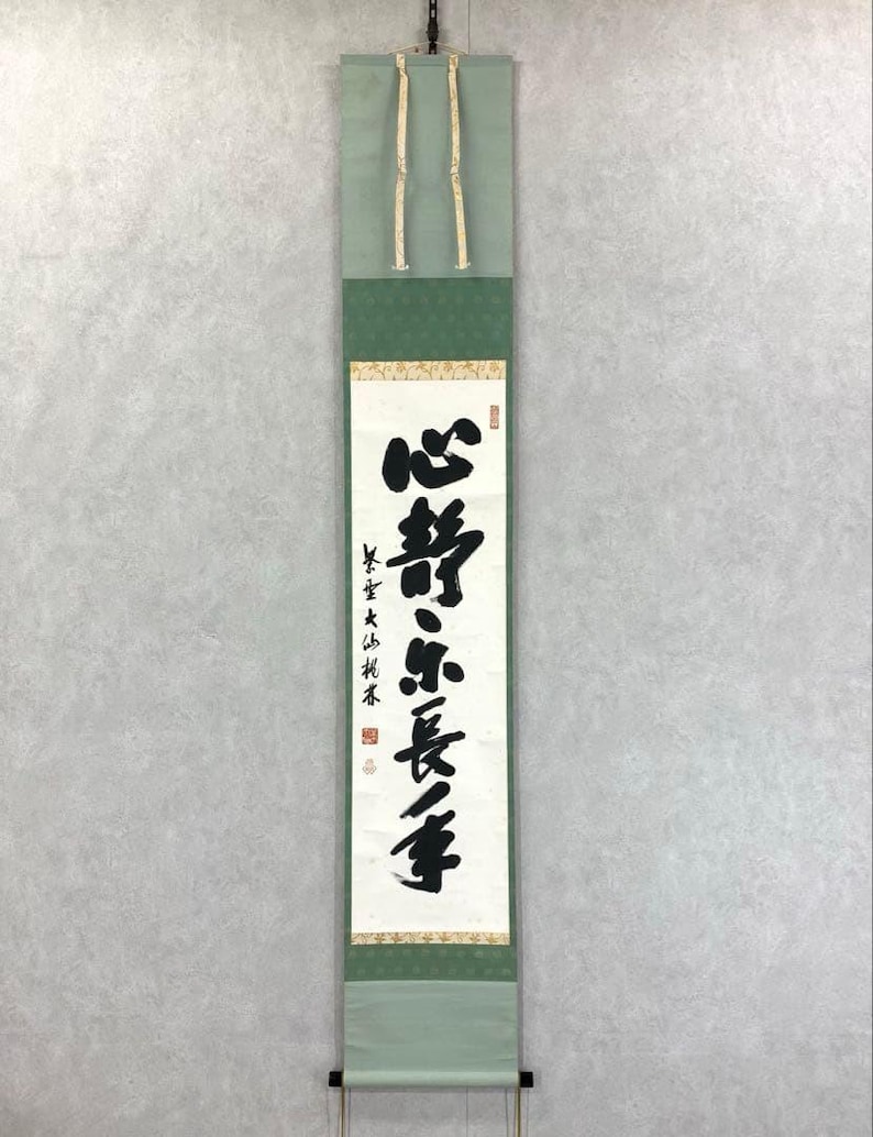 Puede incluir: Un rollo japon&eacute;s vertical con caligraf&iacute;a negra. El rollo tiene bordes verde claro y verde oscuro, con una secci&oacute;n central de color crema. El texto est&aacute; escrito en un estilo tradicional de Asia Oriental.