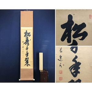 Op de afbeelding: Een verticale Japanse hangrol met zwarte inkt kalligrafie op een lichtbruine papieren achtergrond. De rol bevat een houten stok aan de onder- en bovenkant, met gedetailleerde close-upweergaven van de penseelstreken en rode zegelstempels.