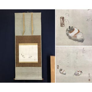 May include: A traditional Japanese scroll painting. The scroll has a light beige fabric top and bottom with a brown patterned middle section. The painting shows two small, stylized figures with calligraphy.