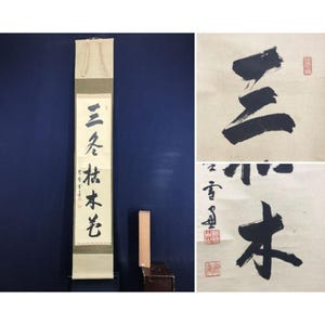 May include: A vertical scroll with Japanese calligraphy in black ink, featuring a cream-colored top and bottom with a central section of text. The image also includes two additional calligraphy pieces with red seals and a small wooden box.