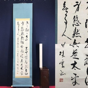 May include: A traditional Japanese scroll with calligraphy in black ink on cream-colored paper. The scroll is mounted on a light blue fabric with wooden dowels at the top and bottom. The calligraphy features vertical text.