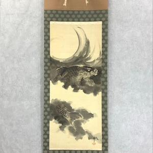 Op de afbeelding: Japans rolschilderij met twee koi-karpers in een donkere, bewolkte omgeving. Het kunstwerk gebruikt tinten grijs en zwart, met een beige achtergrond. De rol heeft een bruine boven- en onderkant met een groen patroon.