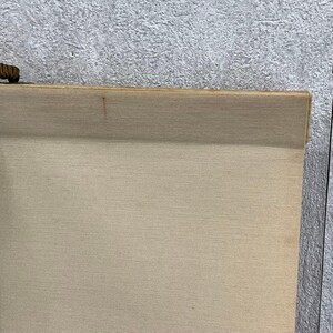 May include: A beige scroll with a wooden top and bottom. The scroll is made of a textured fabric and has a small, dark brown wooden piece attached to the top. The background is a textured gray surface.