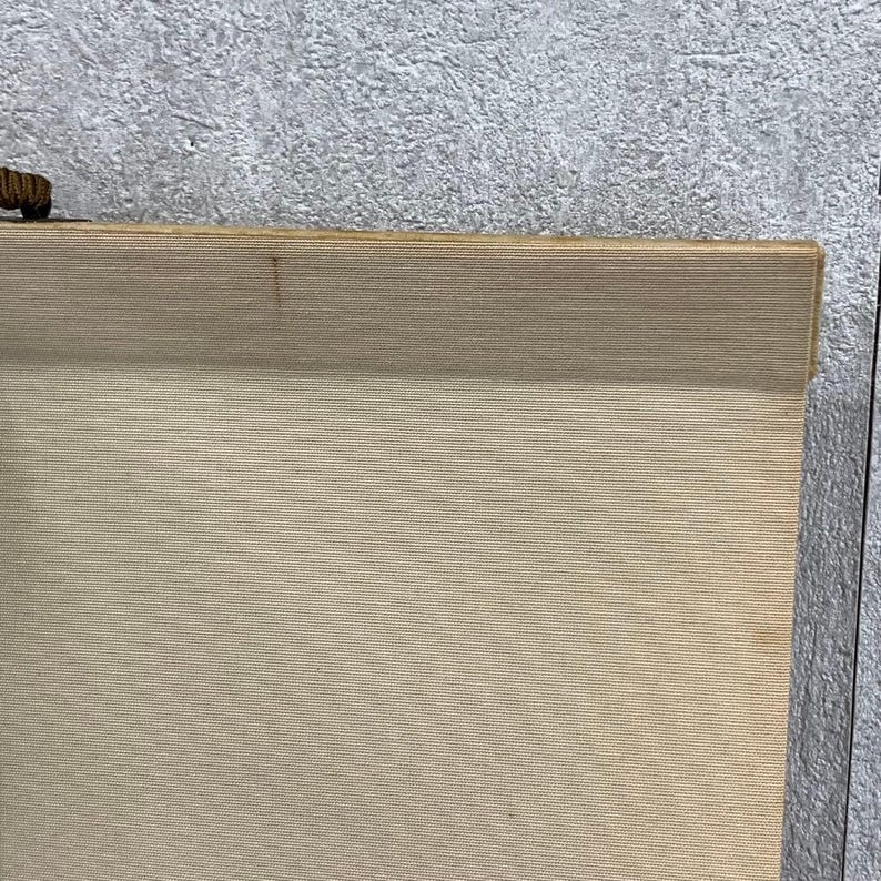 May include: A beige scroll with a wooden top and bottom. The scroll is made of a textured fabric and has a small, dark brown wooden piece attached to the top. The background is a textured gray surface.