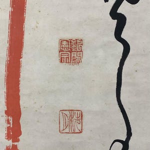 May include: Abstract artwork featuring a vertical red stripe on the left and a flowing black ink design on the right. Two red square stamps with intricate characters are present, adding a traditional touch to the composition. The background is off-white.