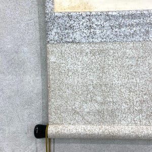 May include: A rolled-up scroll with a black wooden handle and a gold-colored cord. The scroll features a textured, off-white surface with a network of fine, dark lines. The top portion has a light gray and white patterned section.
