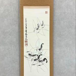 May include: A vertical scroll painting in a minimalist ink wash style. The artwork depicts several shrimp-like figures with delicate lines and brushstrokes. The scroll is framed in a brown border with Japanese text and seals.
