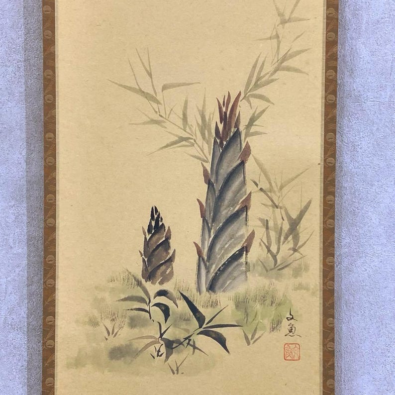 May include: Watercolor painting of bamboo shoots in shades of brown, gray, and green. The artwork features two main shoots, with bamboo leaves in the background. The painting is on a beige background with a brown border.