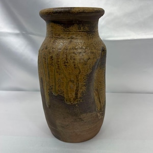 May include: A handcrafted, textured ceramic vase with a brown and tan color scheme. The vase has a cylindrical shape with a slightly flared rim. The exterior features a dripped glaze effect, adding visual interest to the piece.