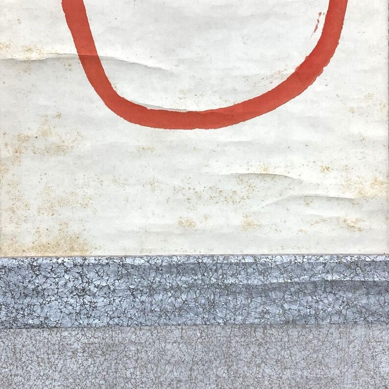 May include: Abstract artwork featuring a large, curved red line against a textured, off-white background. The lower portion displays a textured, gray and blue horizontal band. The piece has a minimalist aesthetic.