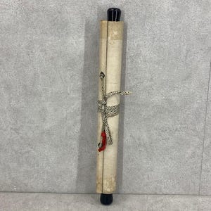 May include: A rolled parchment scroll with black wooden end caps. The scroll is tied with a patterned cord and a red tassel. The paper has a yellowed, aged appearance, suggesting it is vintage or antique.