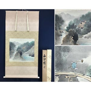 Peut inclure: Peinture sur rouleau japonaise traditionnelle représentant un paysage avec des montagnes, une rivière et des personnages. L'œuvre est encadrée d'un tissu rose clair et d'une bordure beige. Une boîte en bois avec du texte japonais est incluse.