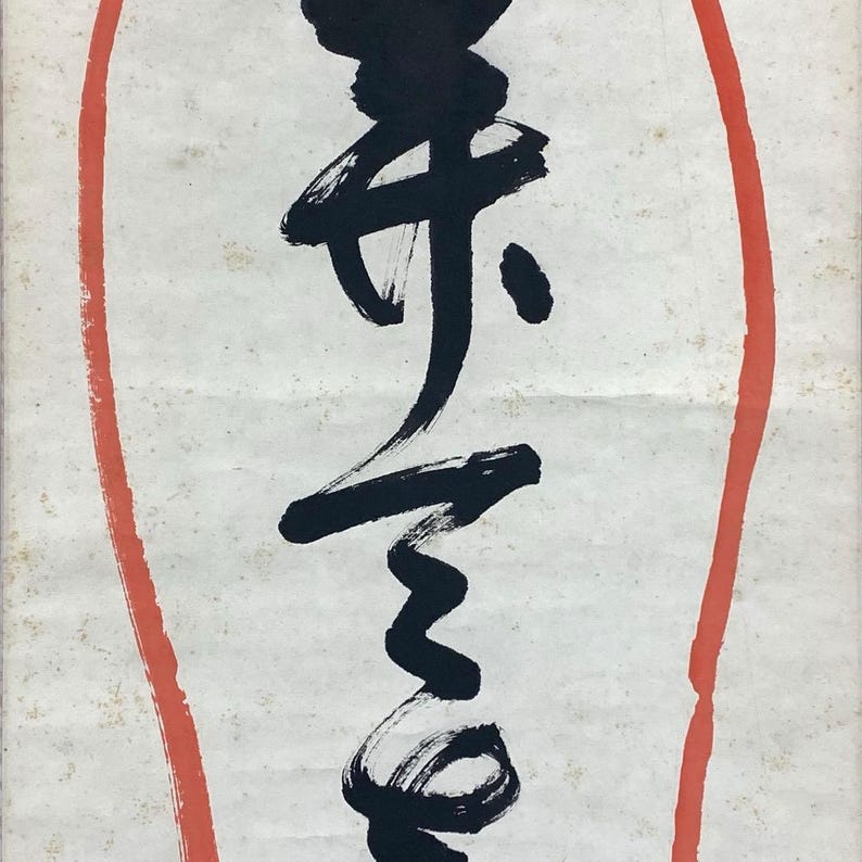 May include: A close-up of a piece of art featuring black calligraphy on a white background. The calligraphy is enclosed within a red oval border. The paper has a slightly aged appearance.