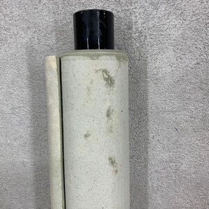 May include: A rolled-up, off-white scroll with a black cylindrical cap. The scroll has visible staining and a slightly aged appearance. The cap is glossy and smooth, contrasting with the textured scroll.