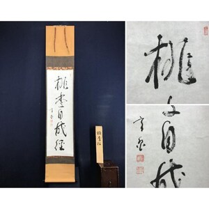以下が含まれることがあります： 黒インクの文字が書かれた日本の書道巻物。巻物の上部と下部はベージュ色で、中央のパネルは白です。テキストが書かれた小さな木片も写っています。