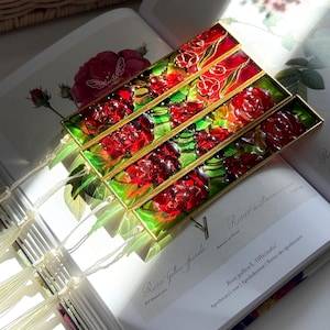 May include: Four rectangular bookmarks with a floral design. Each bookmark has a gold frame with red roses and green leaves. The bookmarks are on an open book with botanical illustrations and text. The book is open to page 202.