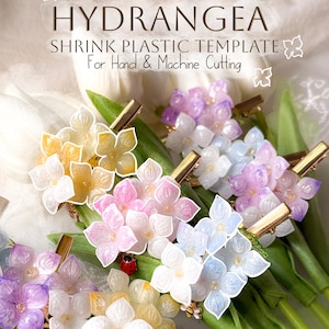 Puede incluir: Horquillas para el cabello con forma de hortensias en tonos amarillo, rosa, blanco, azul y morado. Cada horquilla presenta una pinza dorada y un charm, como una mariquita o una abeja. Se puede leer el texto "HYDRANGEA SHRINK PLASTIC TEMPLATE".